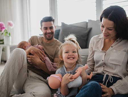 Glückliche junge Familie, die mit einem neugeborenem Baby und einem kleinen Mädchen, die gemeinsame Zeit zu Hause genießen.