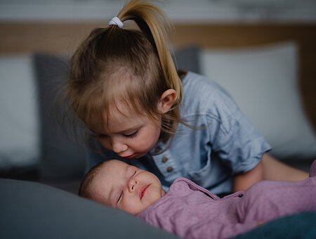 Kleines Mädchen küsst ihre neugeborene kleine Schwester drinnen auf dem Sofa zu Hause.