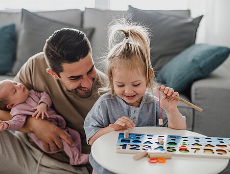 Glücklicher junger Mann, der sich zu Hause um sein neugeborenes Baby und seine kleine Tochter kümmert, Vaterschaftsurlaub.