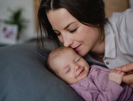 Glückliche junge Mutter küsst ihr neugeborenes Mädchen, das zu Hause auf dem Sofa liegt.